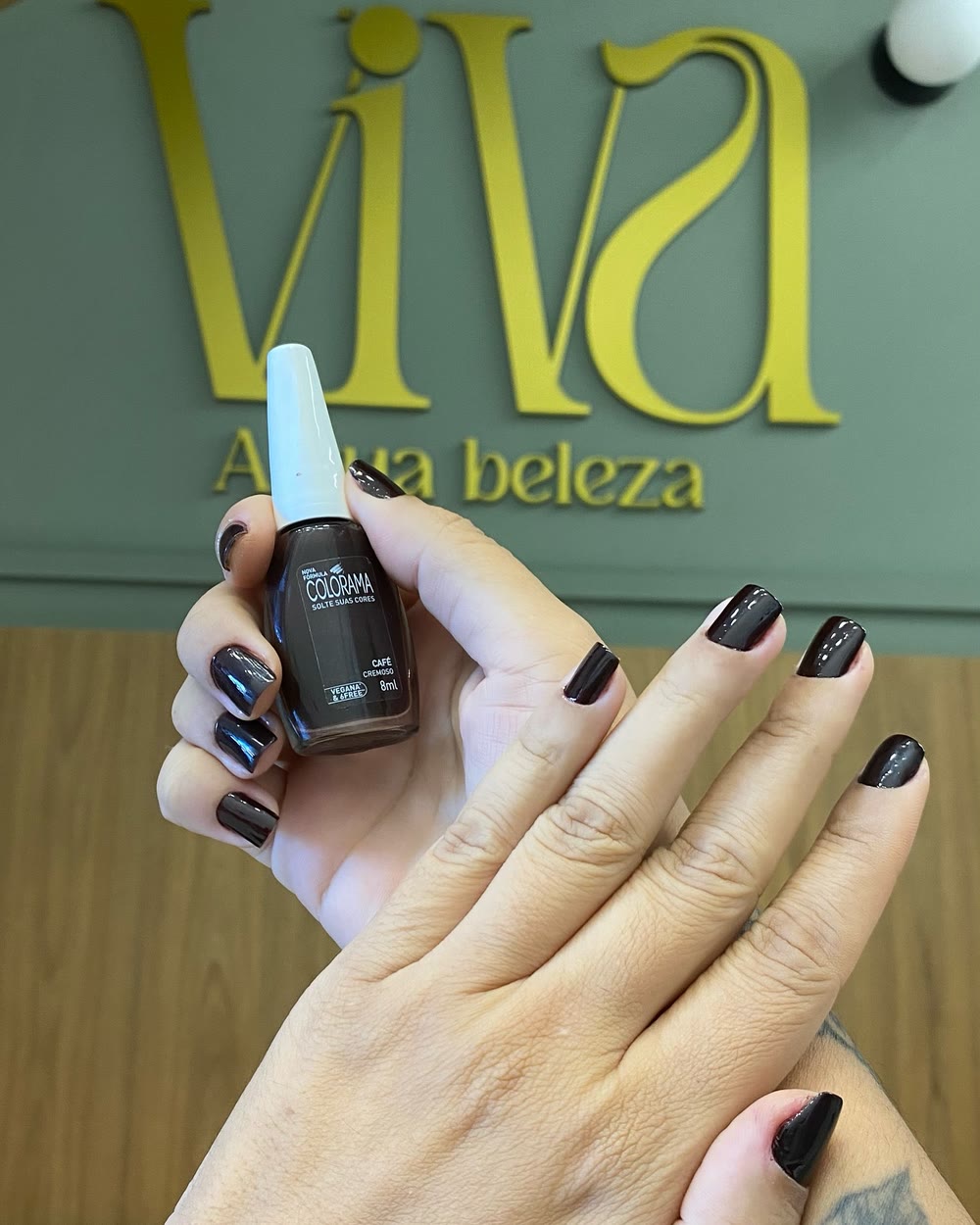 As mesmas mãos com as unhas esmaltadas em marrom café